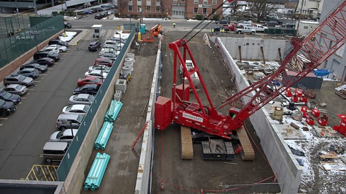 Professional crane operator demonstrating Crane Operations Supporting Confined Space Work techniques on an active construction site - essential knowledge for NCCCO certification exam preparation covering confined space crane safety protocols and operational procedures